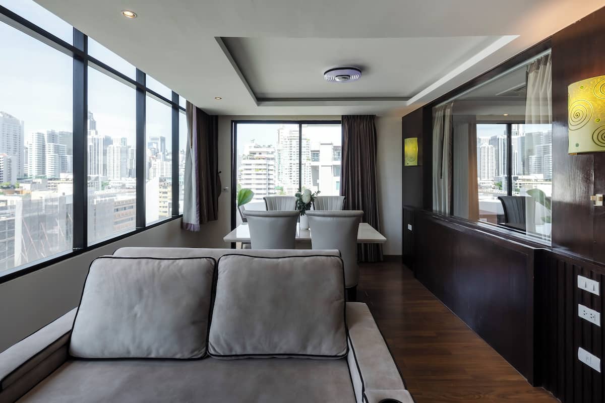 Ein modernes Hotelzimmer mit großem Fenster, einer Couch, einem Essbereich und Blick auf die Stadtlandschaft.