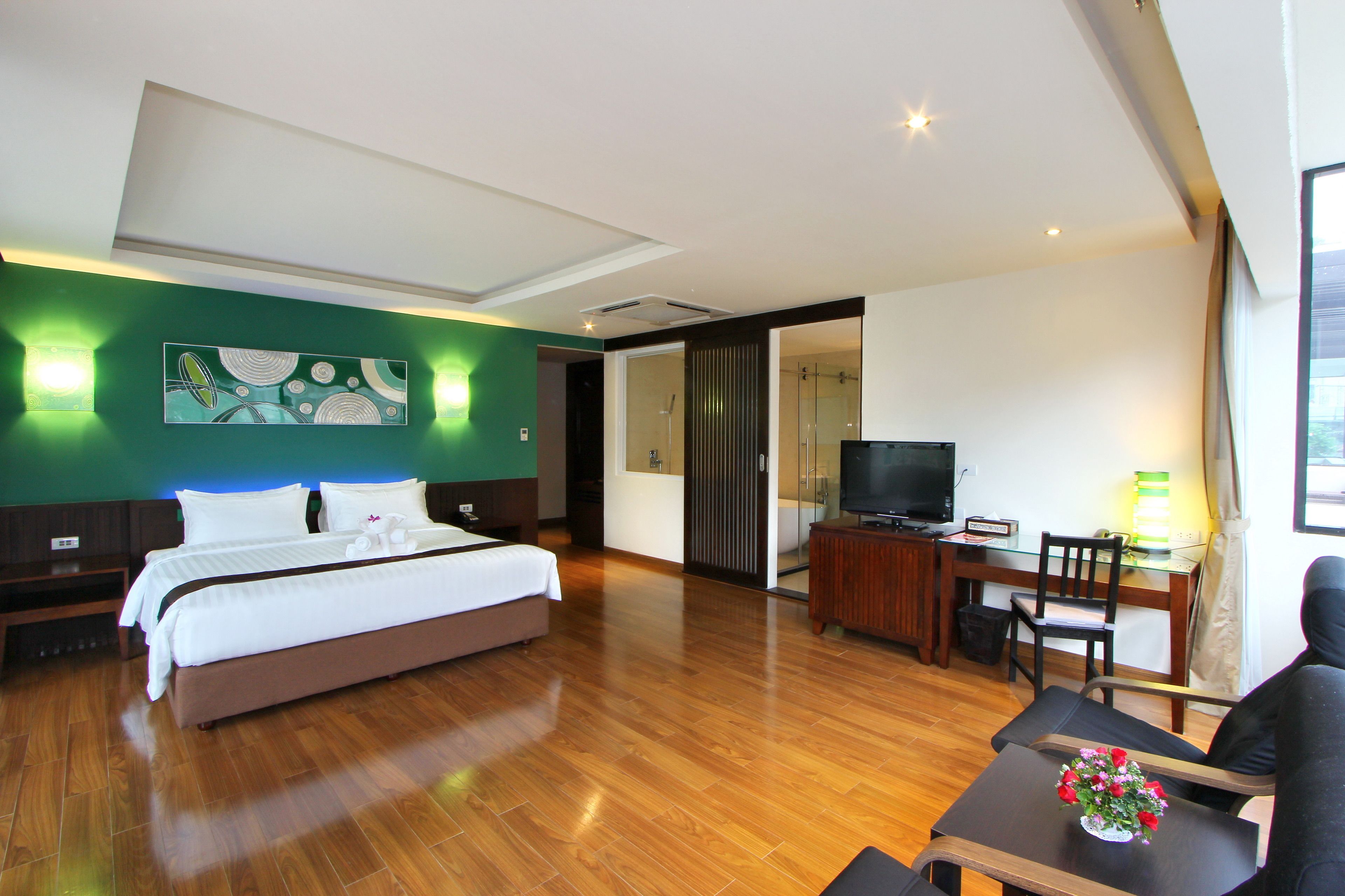 A hotel room with a bed, a desk with a computer, a TV, and a seating area with a table and chairs.