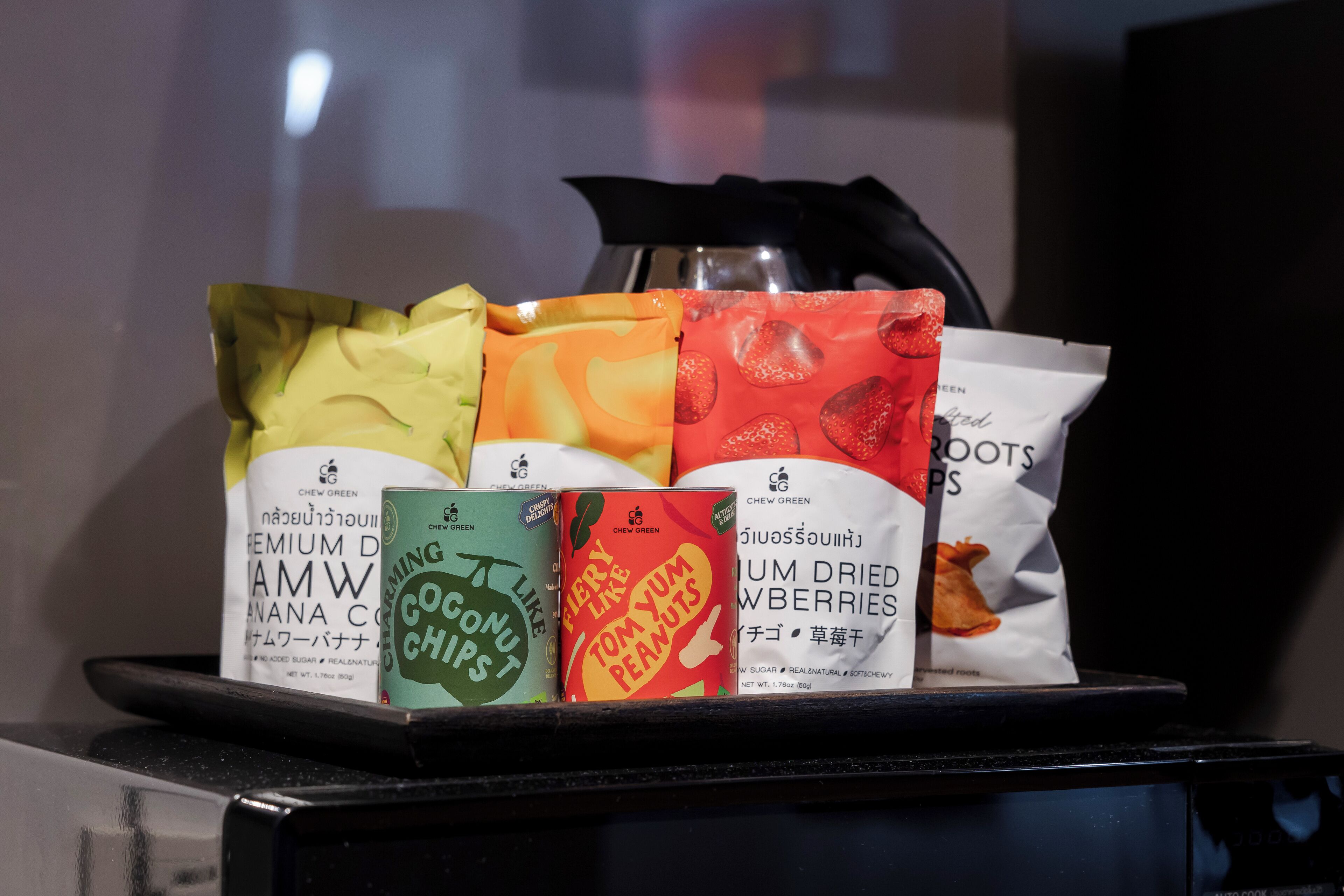 A display of various snack packages including coconut chips, Tom Yum Peanuts, and dried strawberries.