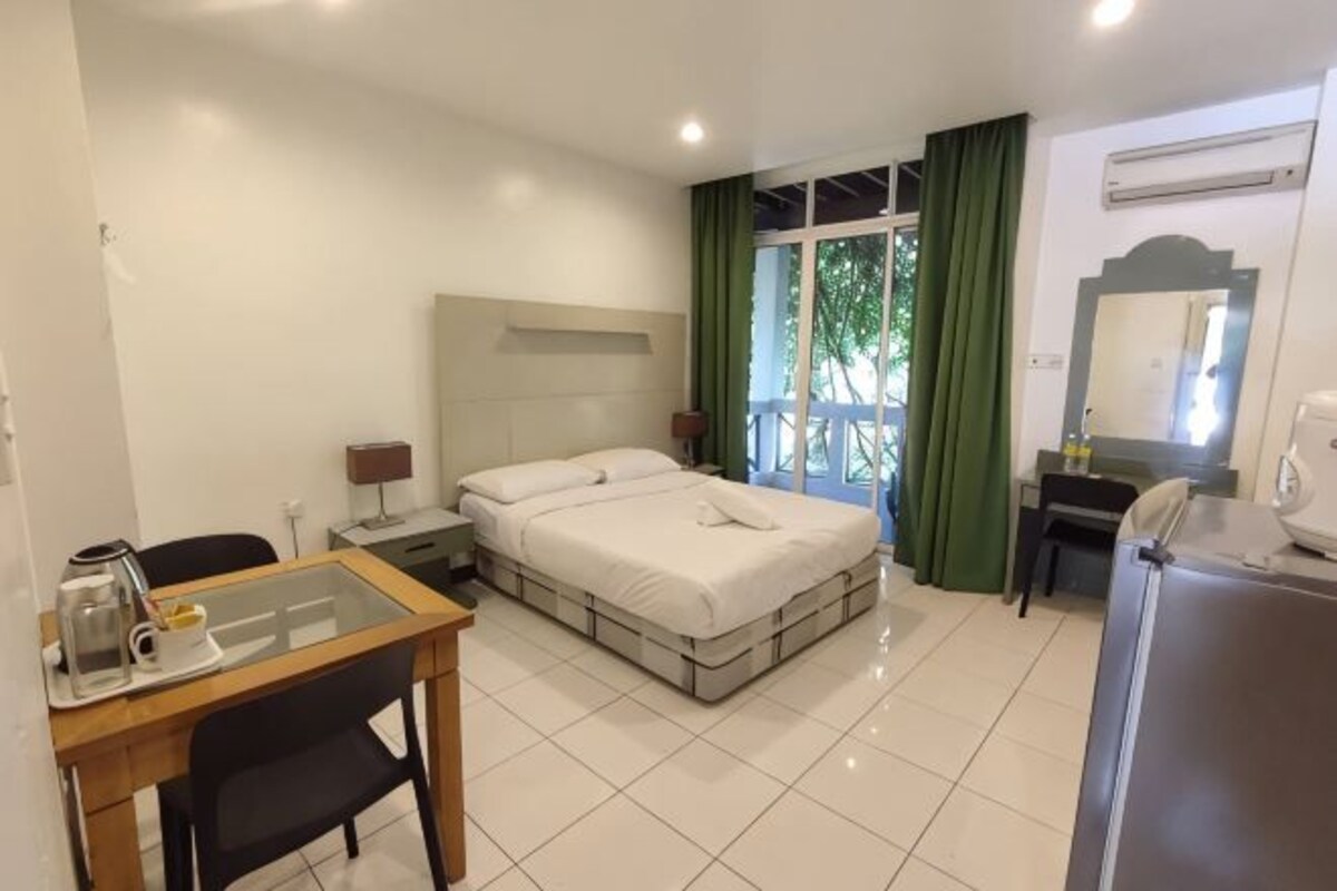 A hotel room with a bed, a desk, a chair, a refrigerator, a mirror, and a window with curtains.