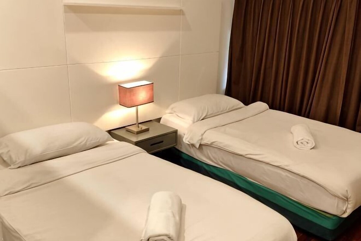 A hotel room with two beds, a nightstand with a lamp, and a curtain.