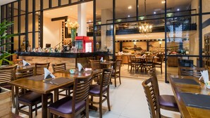 A restaurant with wooden tables and chairs, a bar area, and a view of the Eiffel Tower through large windows. - Mercure Salvador Boulevard (Salvador)