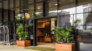 A modern hotel entrance with large glass windows, indoor plants, and a seating area visible through the doorway. - Mercure Salvador Boulevard (Salvador)