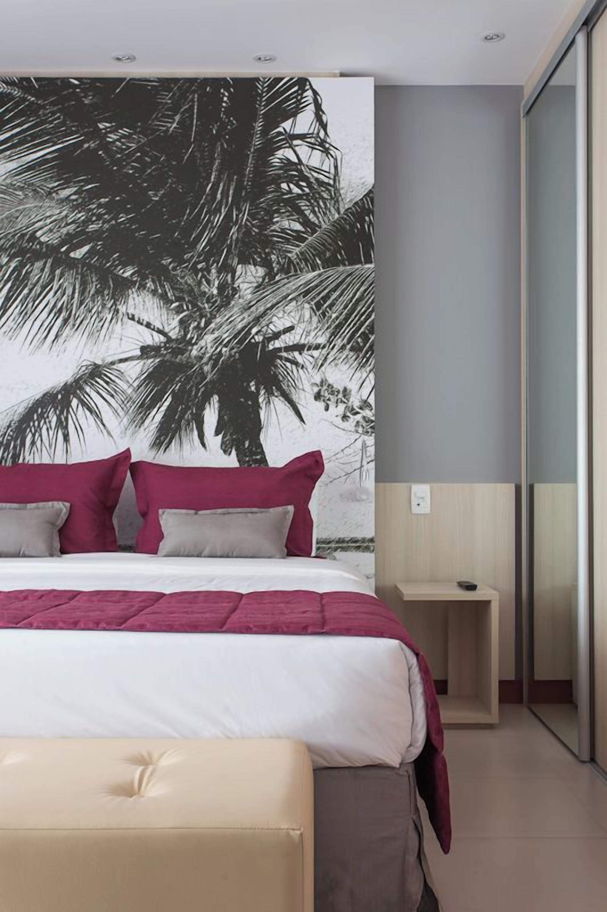 Una camera da letto con un letto, un comodino, una panca e un grande murale raffigurante palme.