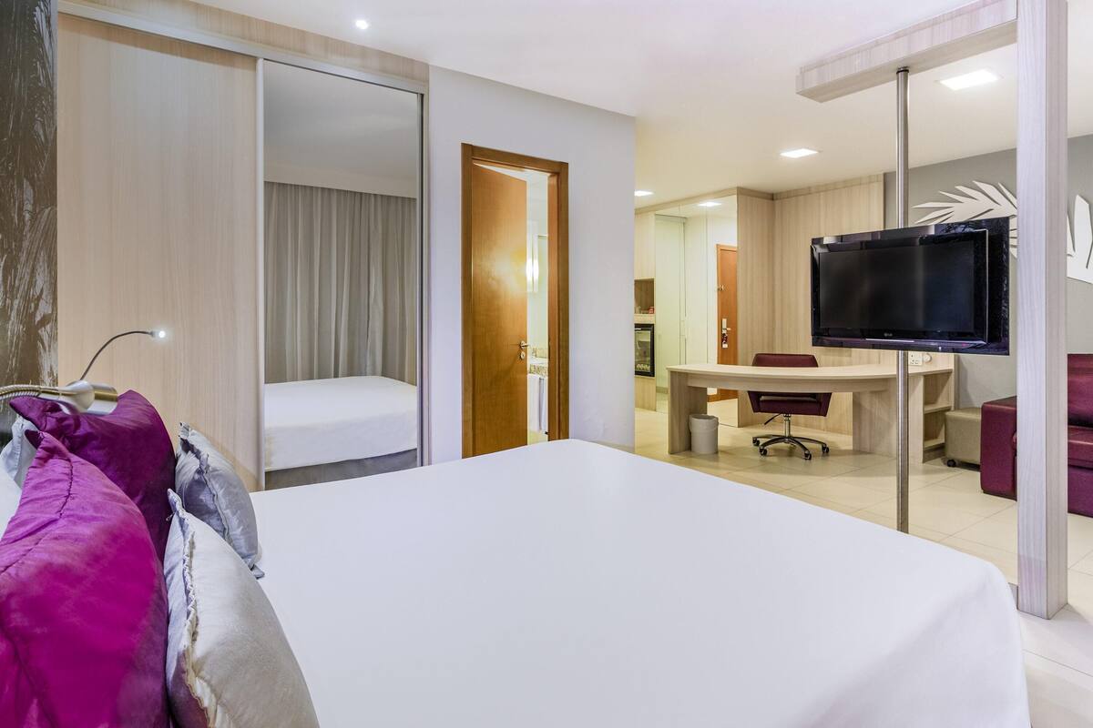 A hotel room with a bed, a desk, a chair, a TV, and a bathroom.