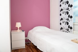 A bedroom with a white bed, a nightstand with a lamp, and a wall with a black and white abstract pattern. - Center Hotel (Tallinn)