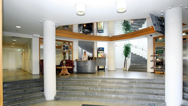 A hotel lobby with a reception desk, a staircase, and a reception area.