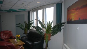 A room with a black leather chair, a red leather chair, a wooden table with a vase of flowers, and two potted plants.