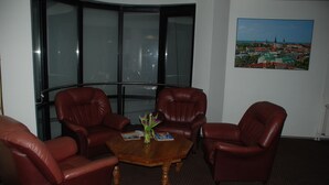 A room with a wooden coffee table, two leather armchairs, a glass partition, and a cityscape painting on the wall.