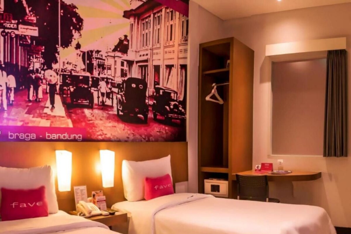 A hotel room with two beds, a wardrobe, a small table, and a wall-mounted TV displaying a cityscape.