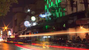 A nighttime street scene with illuminated signs for Heineken, Carlsberg, and Kumpoet Cafe.
