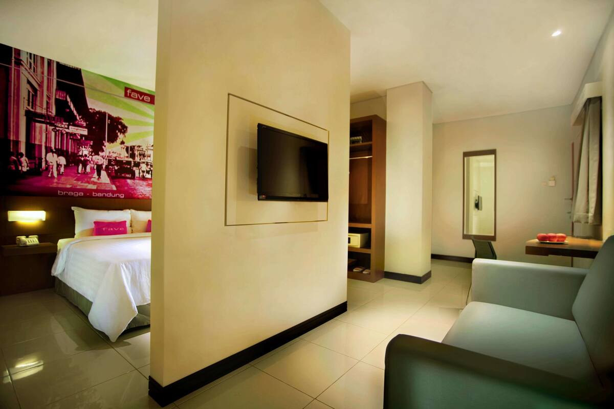 A hotel room with a bed, a TV mounted on the wall, a seating area, and a closet.