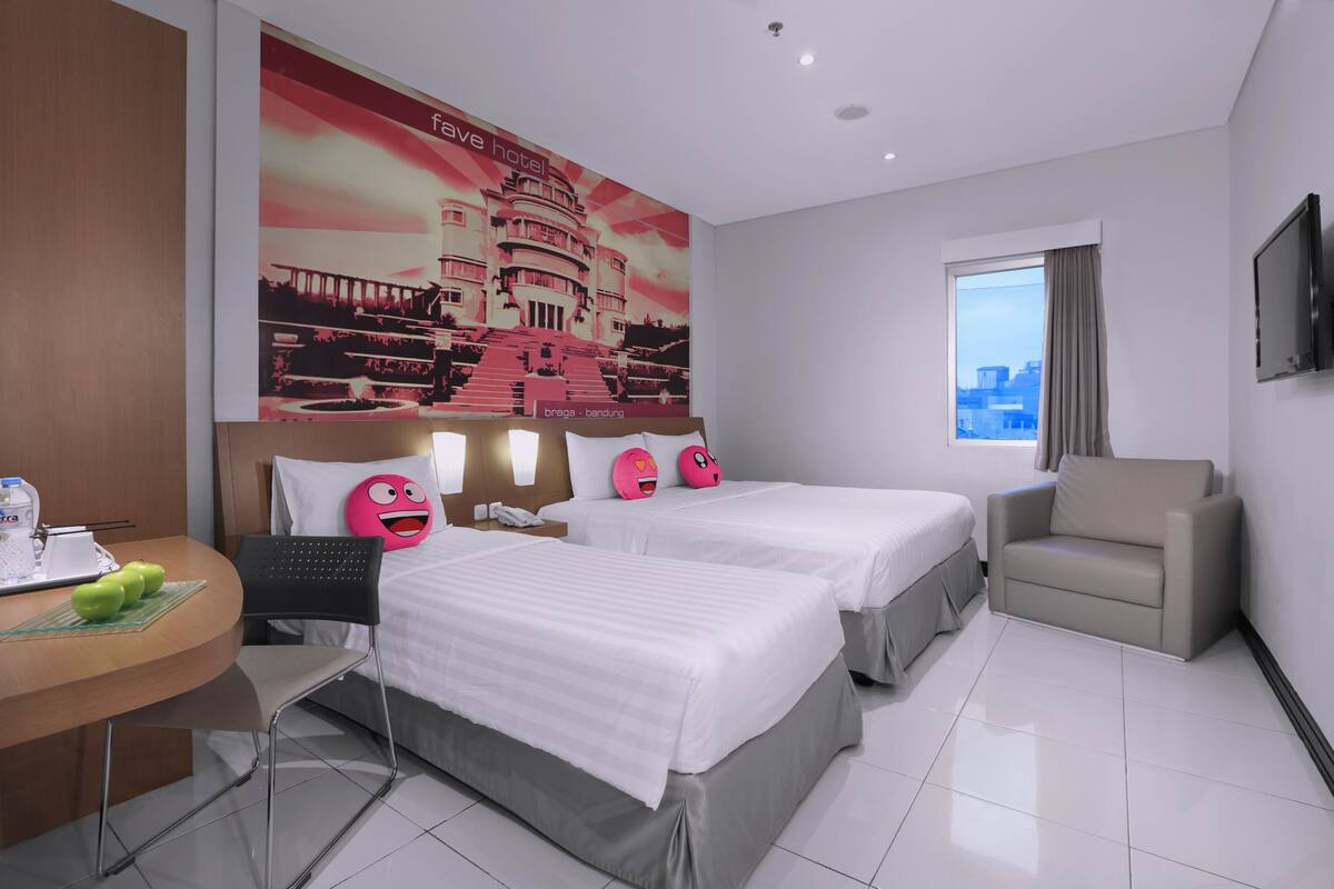 A hotel room with two beds, a desk with a chair, a sofa, a TV, and a large window.