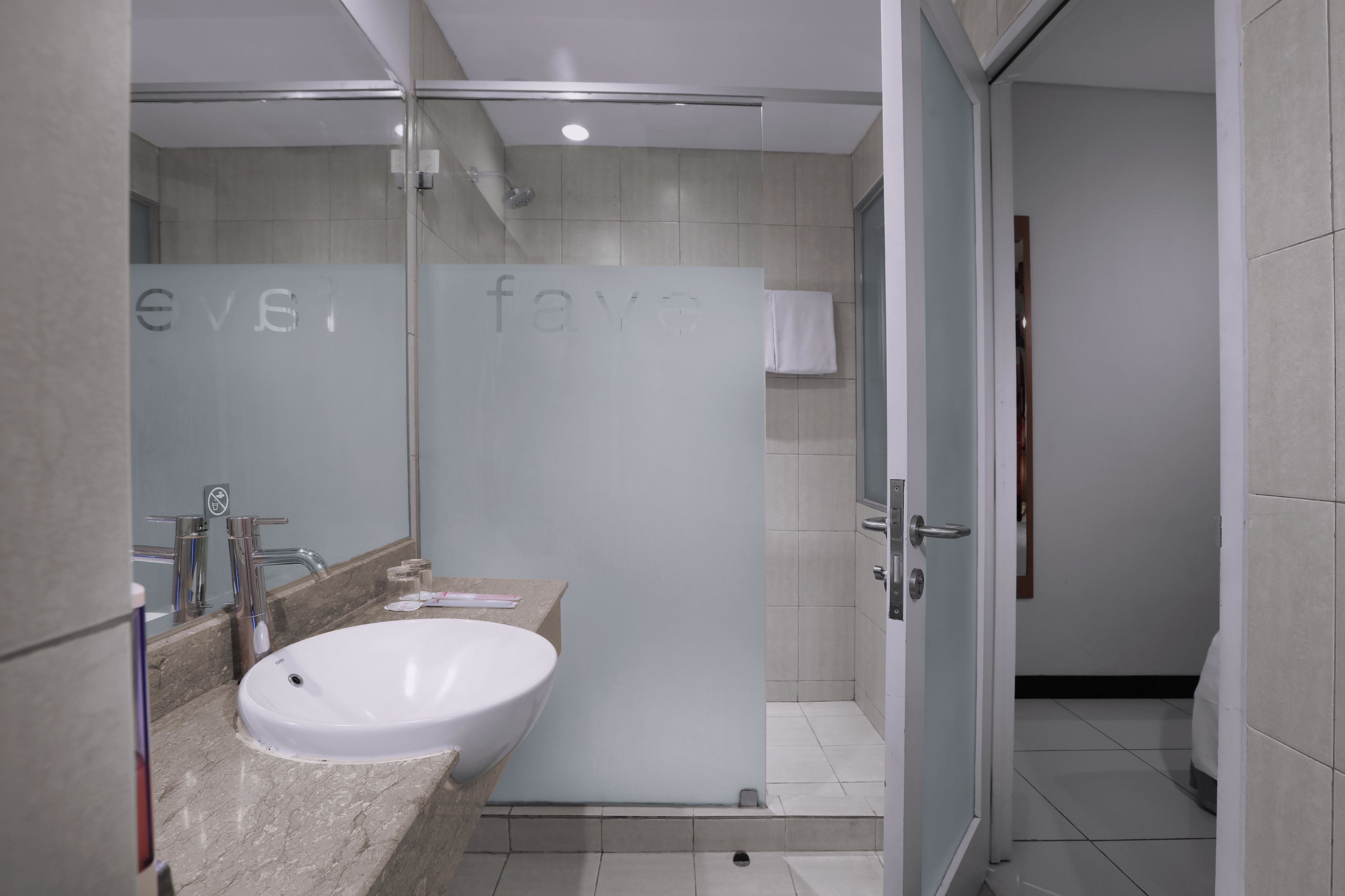 A modern bathroom with a large white sink, a glass shower enclosure, and a frosted glass partition with the word "fave" on it.