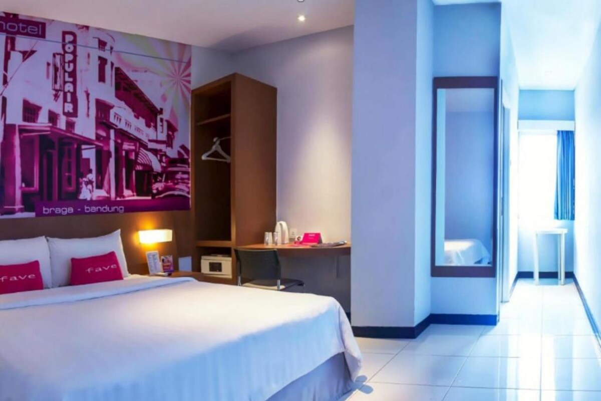 A hotel room with a bed, a desk, a wardrobe, and a large window.