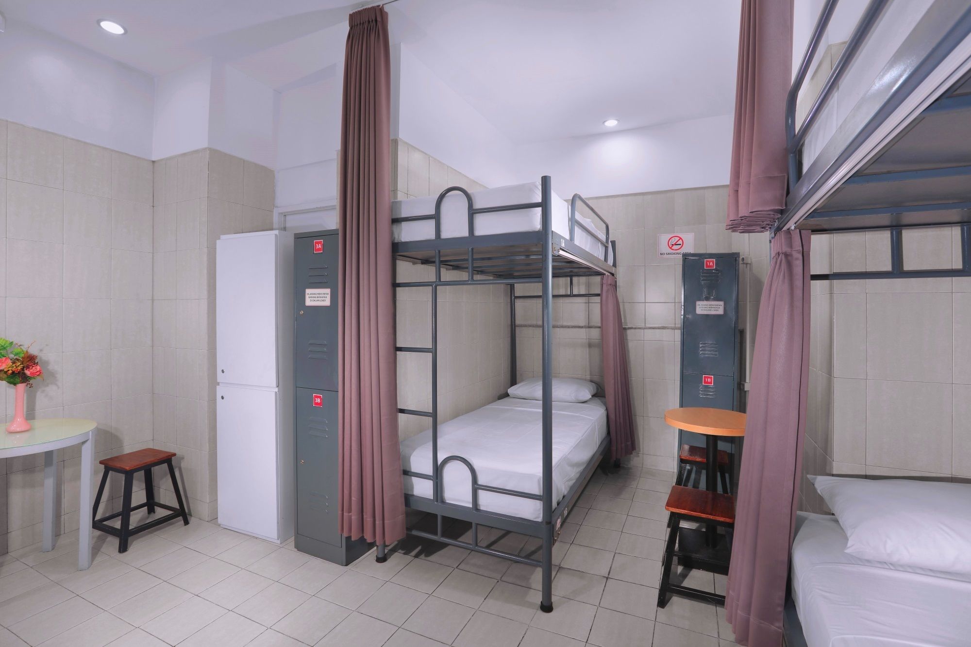 A dormitory room with bunk beds, a desk, a chair, a small stool, and a refrigerator.