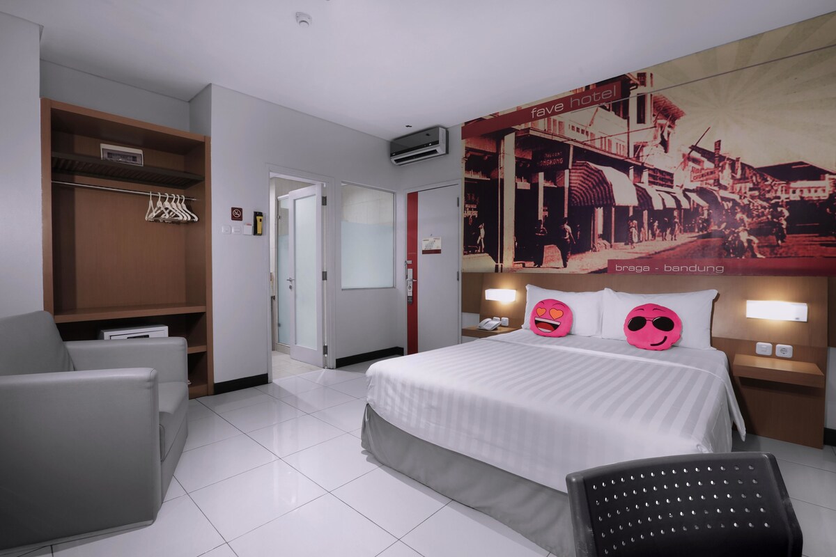 A hotel room with a bed, a desk, a chair, a wardrobe, and a wall with a cityscape poster.