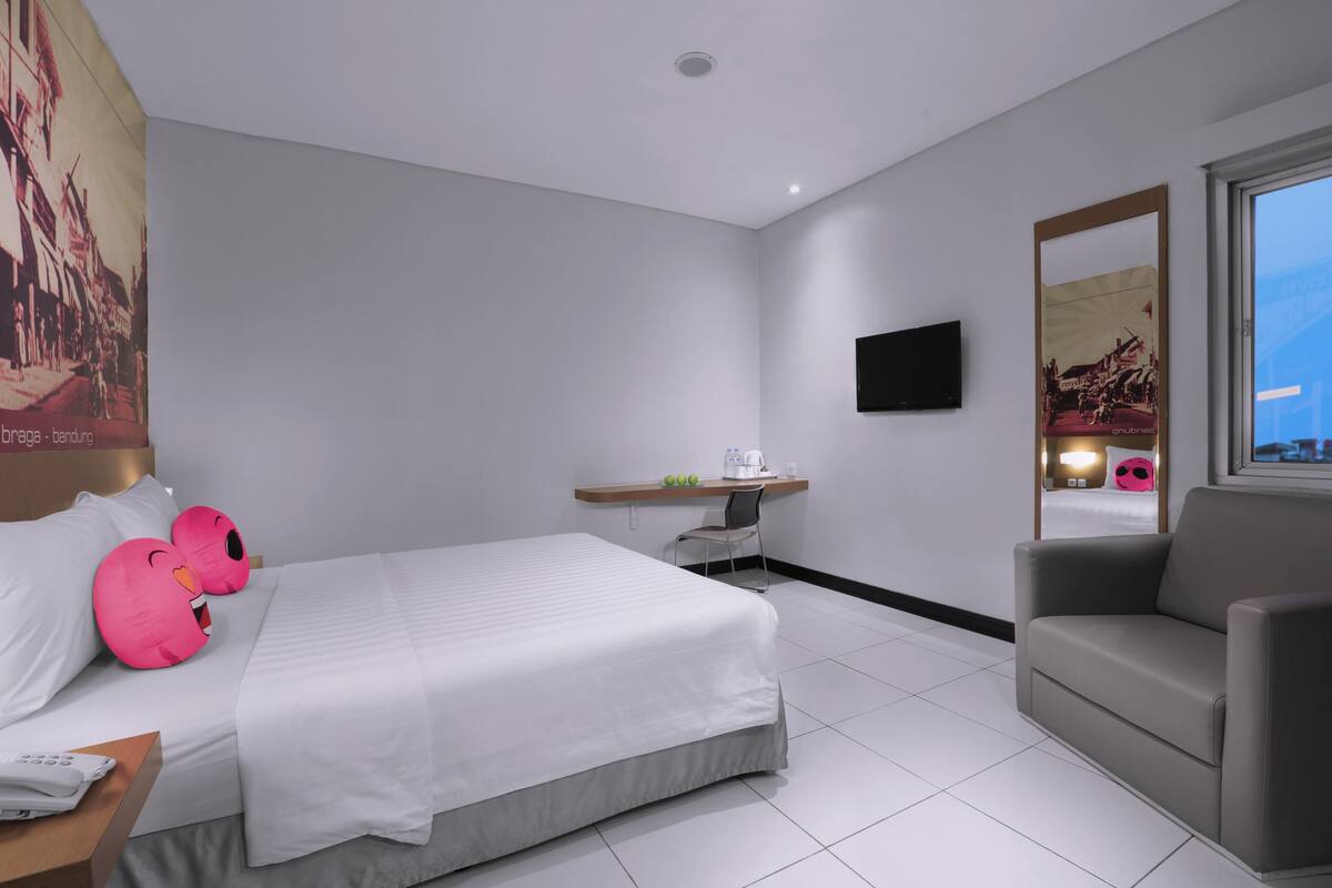 A modern hotel room with a bed, a desk, a chair, and a TV on the wall.