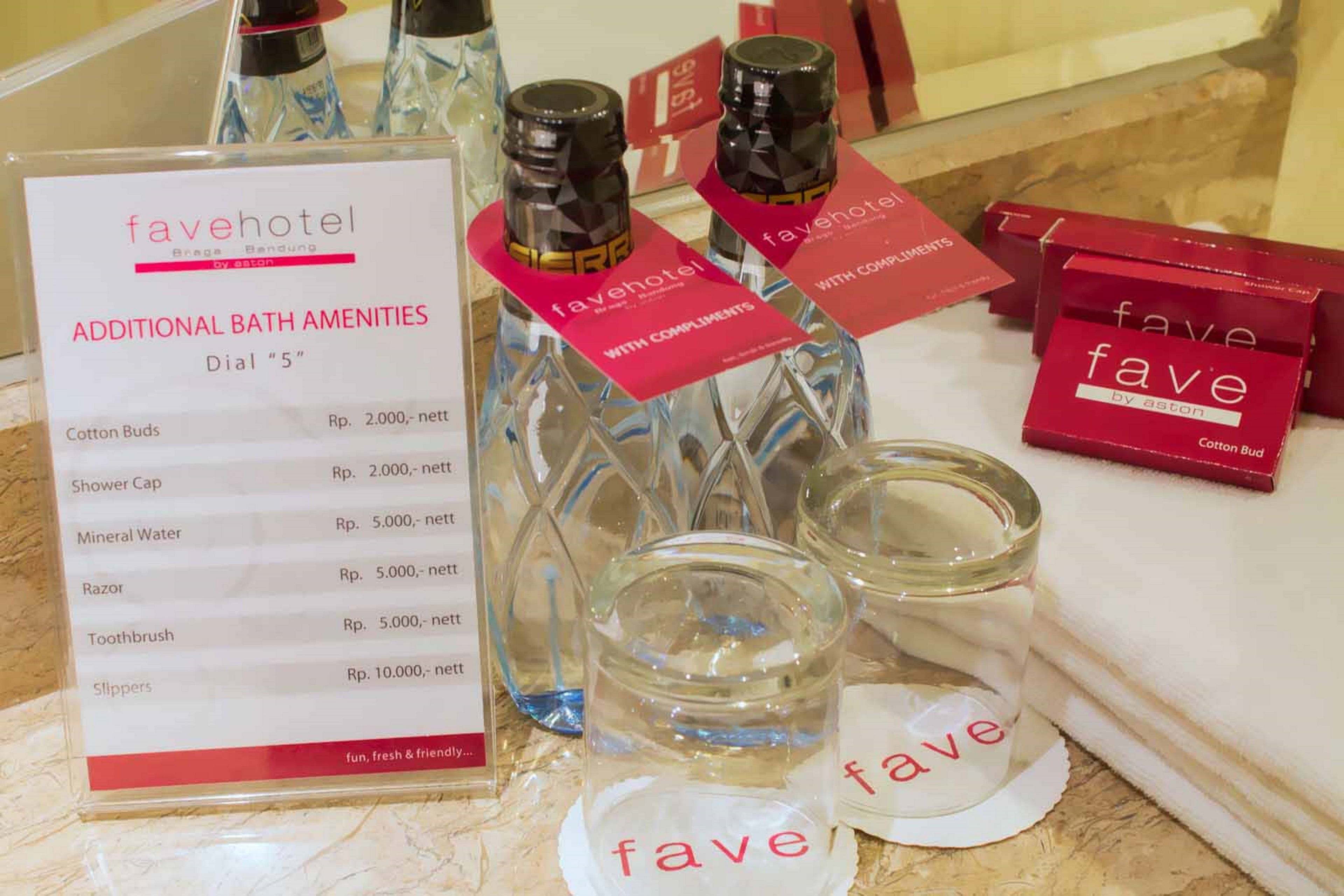 A hotel room with a bath amenities table displaying items like cotton buds, shower cap, mineral water, razor, toothbrush, and slippers.
