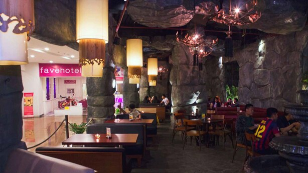 A restaurant with stone walls and hanging lamps, tables and chairs, and a visible 'favehotel' sign. - favehotel Braga (Bandung)