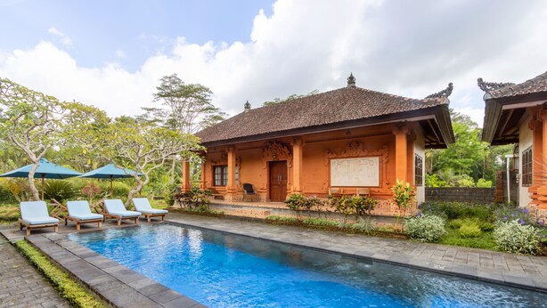 Ein Schwimmbecken mit Liegestühlen und Sonnenschirmen, umgeben von einem Garten und traditioneller Architektur.