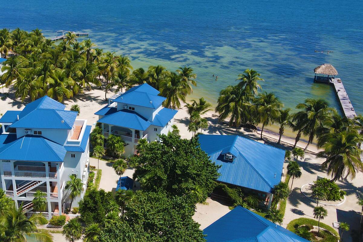 Un resort con varias edificaciones, una playa y un muelle que se adentra en el océano.