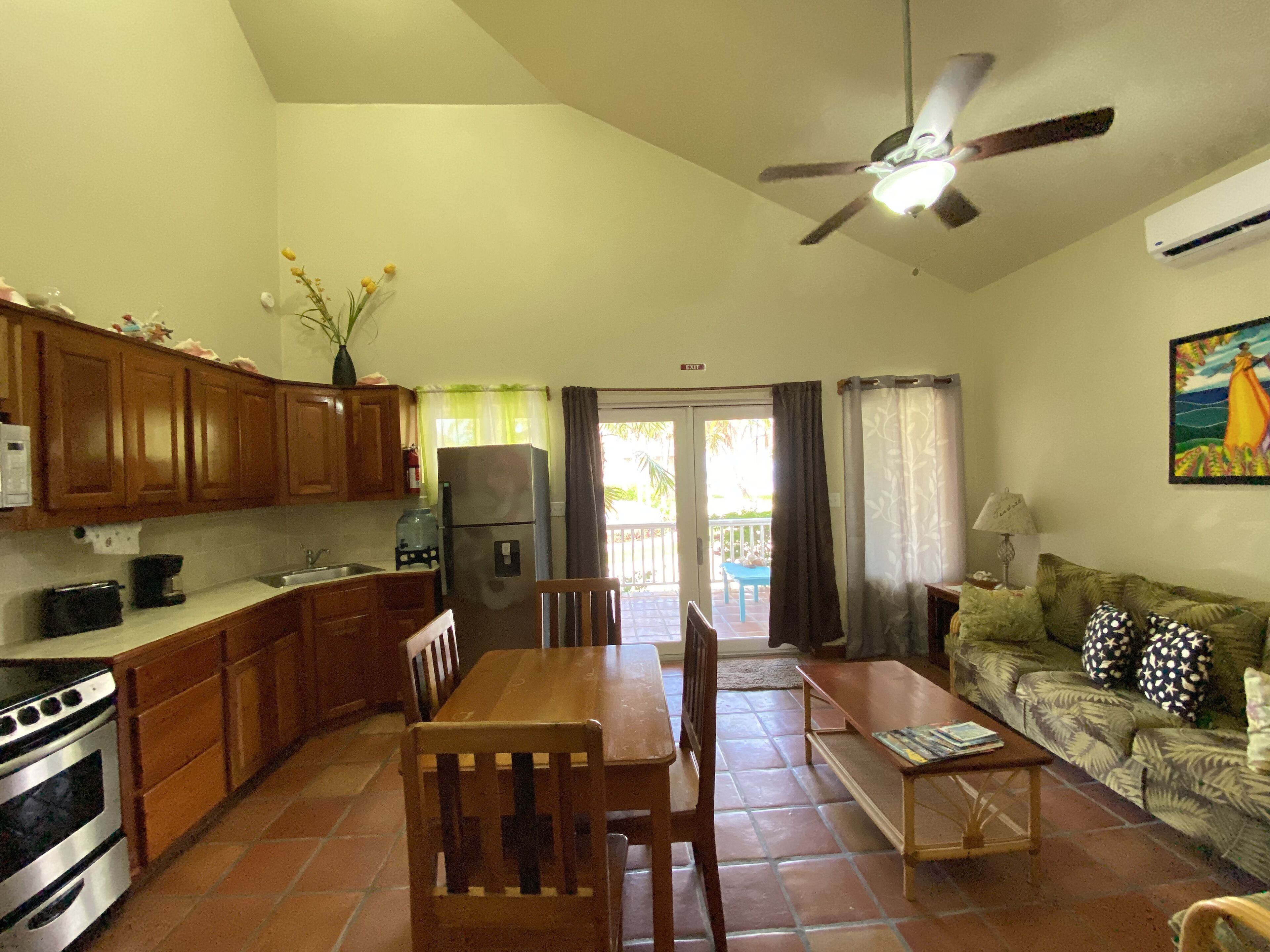 A compact kitchen with wooden cabinets, a refrigerator, and a dining area with a table and chairs.