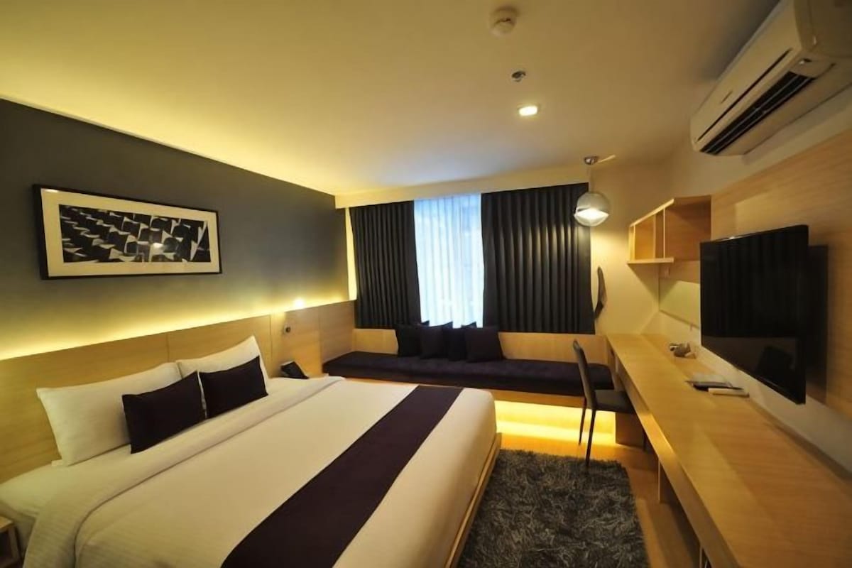 A hotel room with a bed, a desk, a television, and a window with curtains.