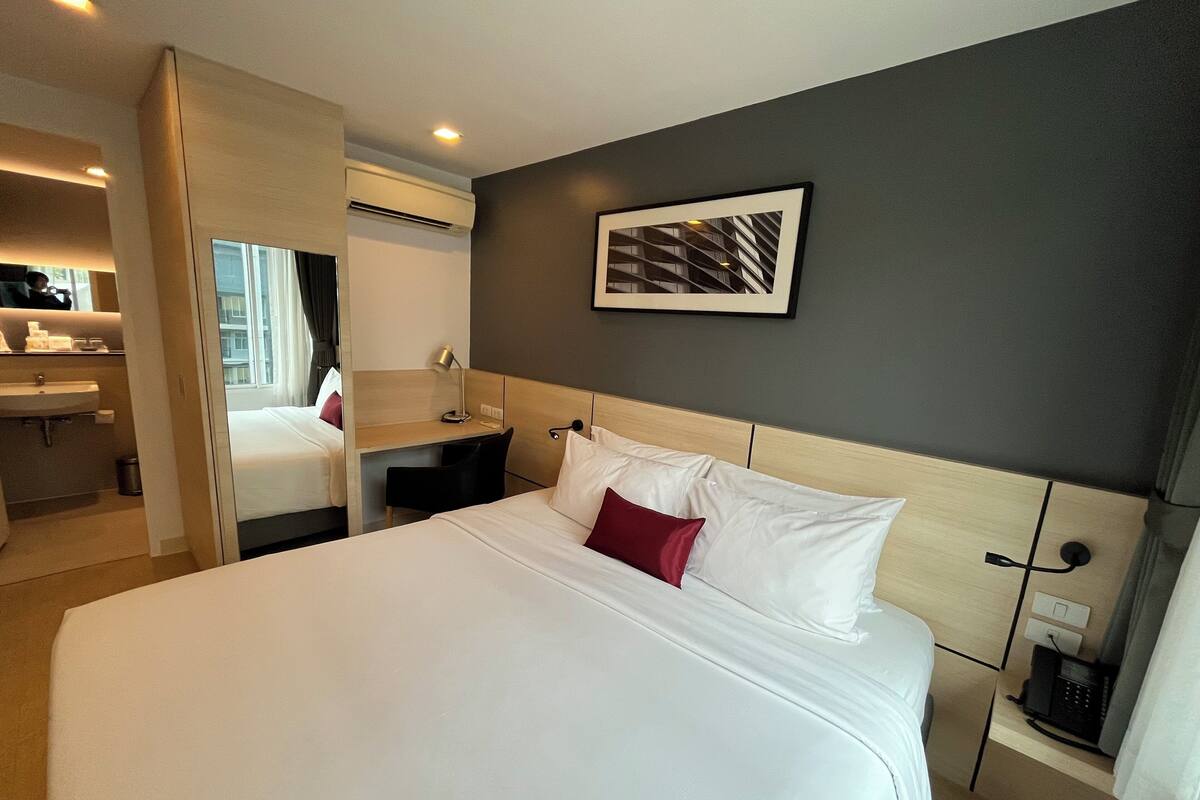 A hotel room with a large bed, a desk, a chair, a bedside table, a phone, and a wall-mounted picture.