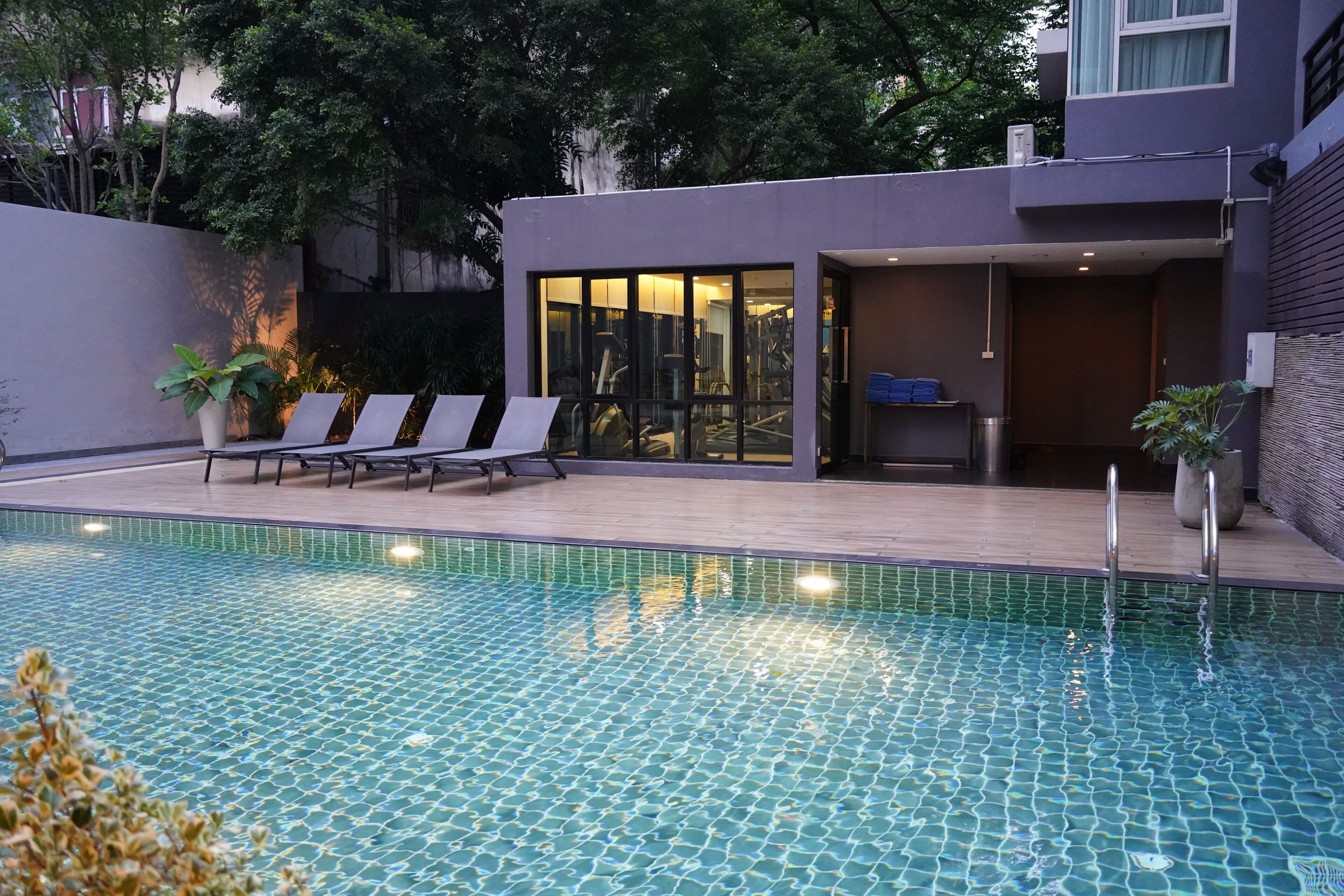 A swimming pool with lounge chairs, a gym, and a modern building with large windows.