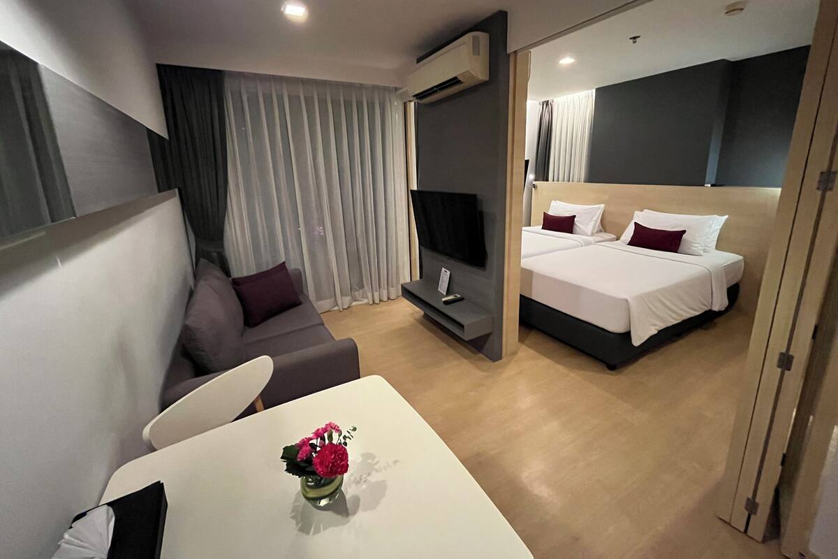 A hotel room with a bed, a sofa, a TV, and a table with a vase of flowers.