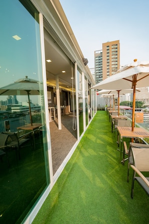 Terraço no telhado com área de estar ao ar livre, parede de vidro e vista da paisagem urbana.