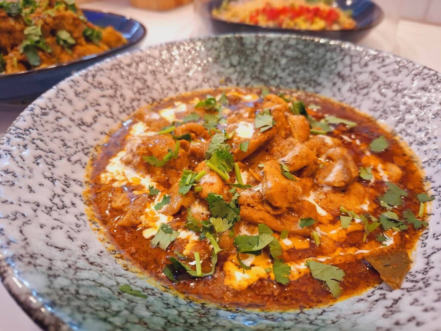 Un plat de curry de poulet, nappé d’une sauce crémeuse et garni d’herbes fraîches.