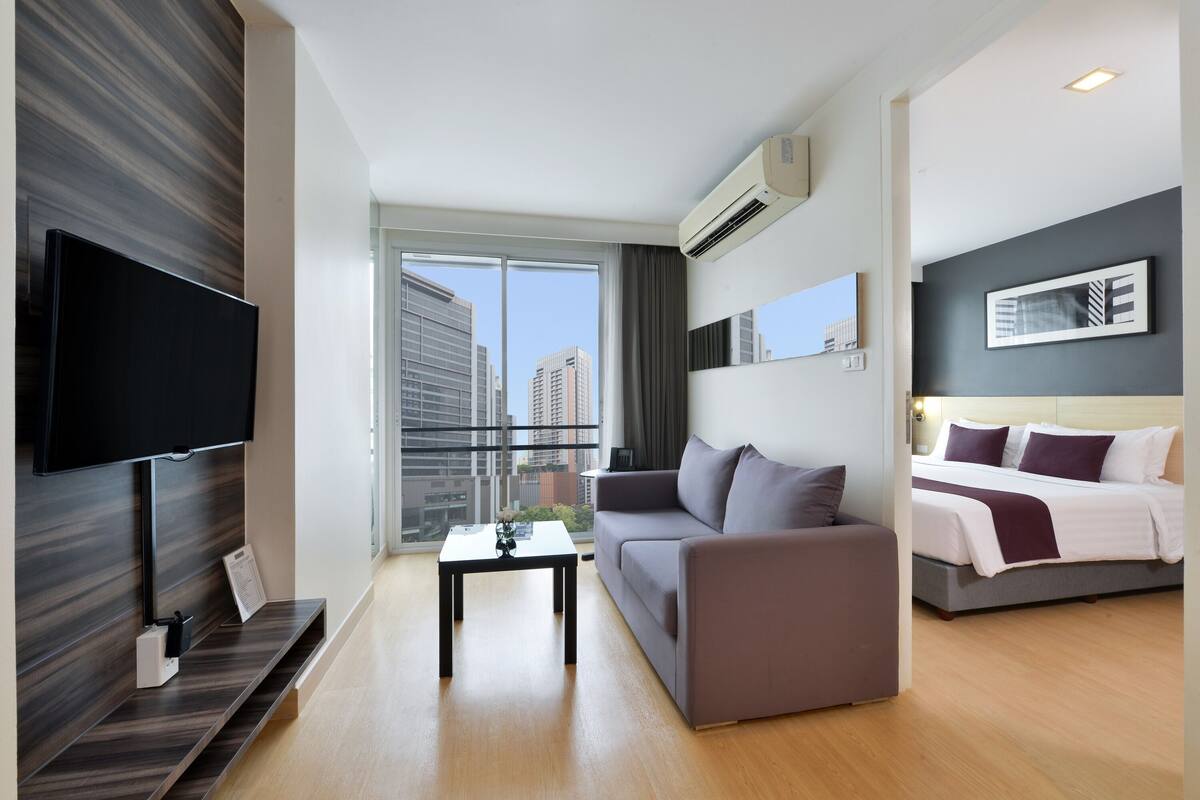 A modern hotel room with a flat-screen TV, a sofa, a bed, and a balcony with a city view.