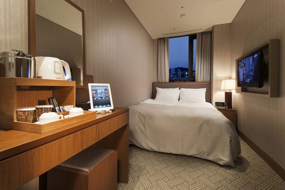 Una habitación de hotel con cama, escritorio, computadora, cafetera y televisión.