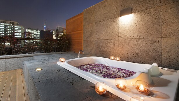 Un área de spa en la azotea con una bañera grande llena de agua y pétalos de rosa, rodeada de velas.