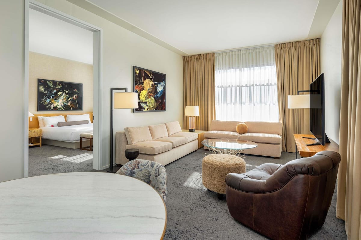 A modern hotel room with a bed, two sofas, a coffee table, a TV, and artwork on the walls.