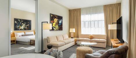 A modern hotel room with a bed, two sofas, a coffee table, a TV, and artwork on the walls.