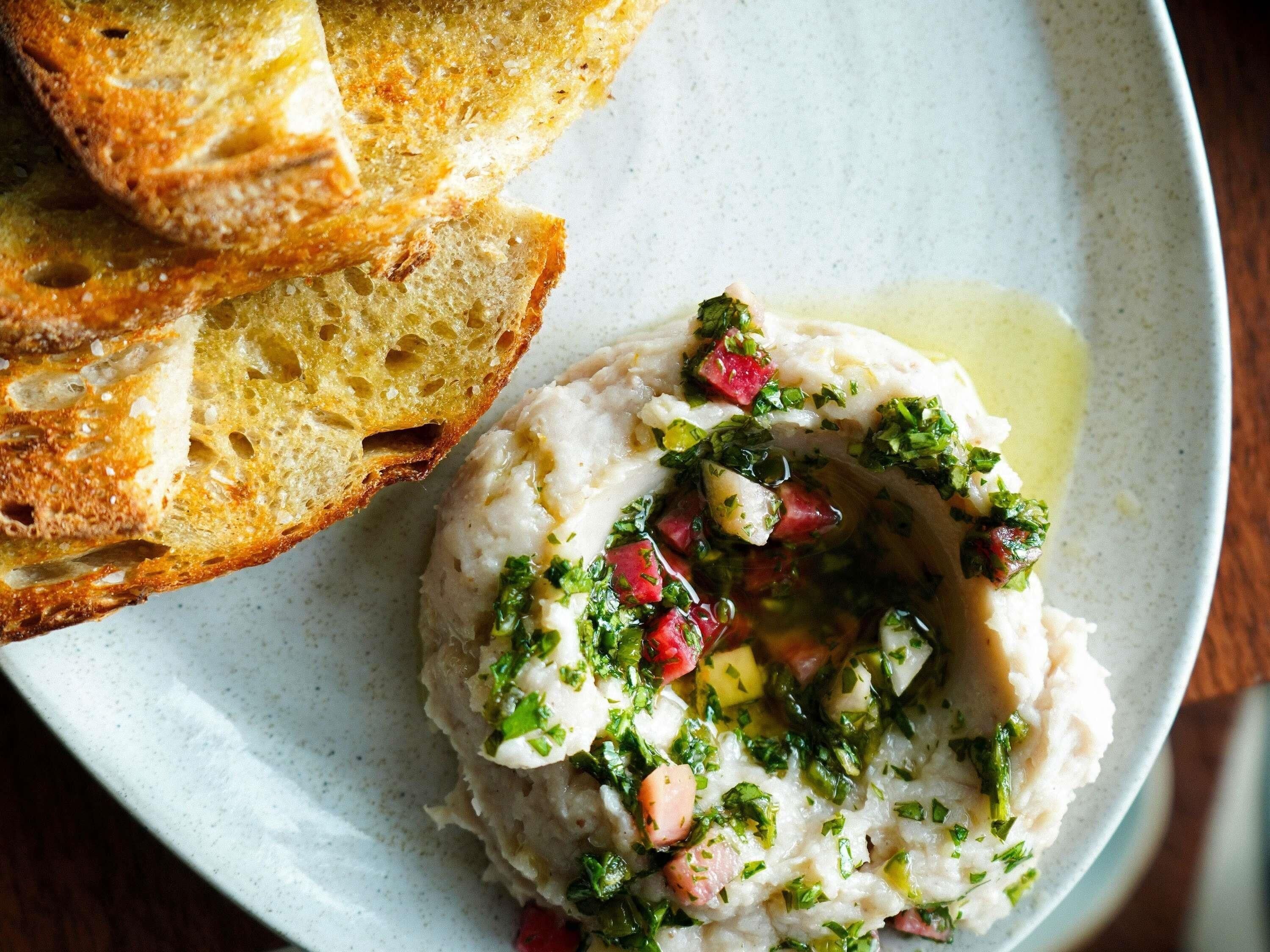 Une assiette contenant un plat crémeux, garni d’herbes et de légumes coupés en dés, accompagné de tranches de pain grillé.