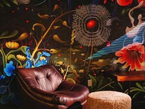 A room with a leather chair, a round ottoman, and a wall with abstract art.
