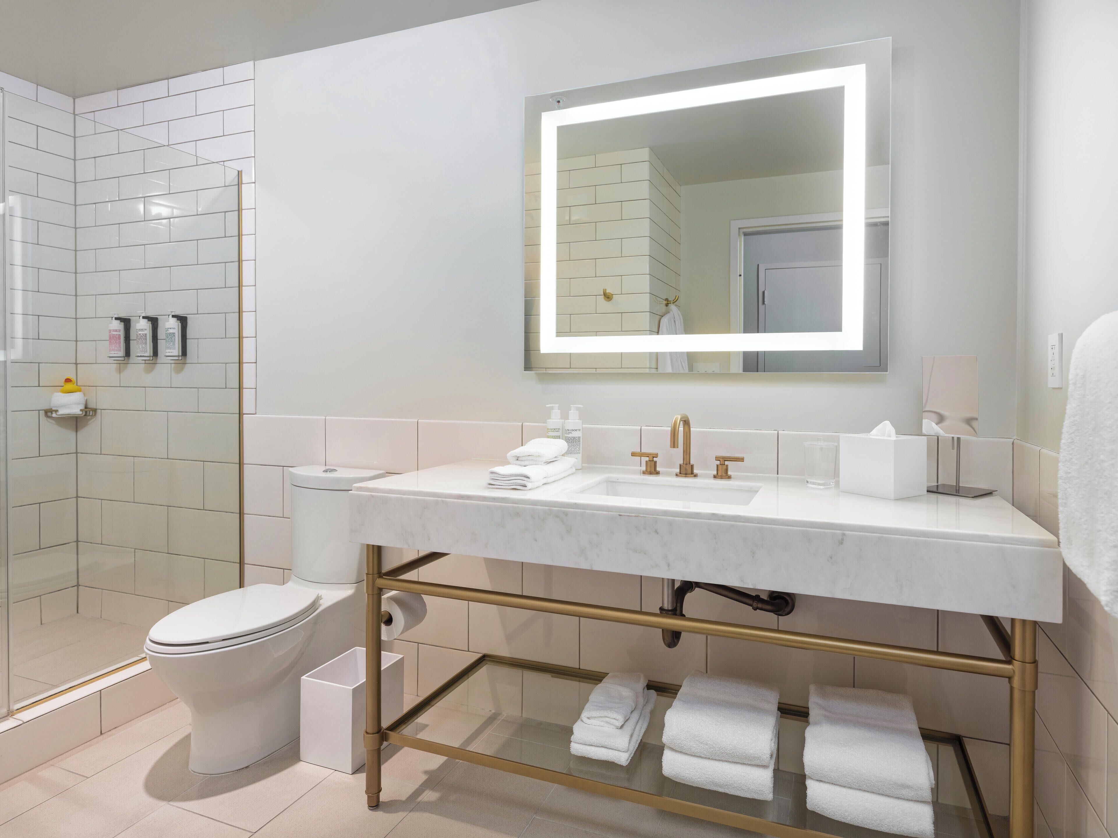 A modern bathroom with a white sink, gold fixtures, and a large mirror.