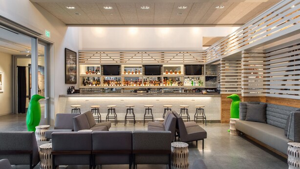 A modern bar area with a long counter, multiple stools, and a seating area with sofas and round tables. - 21c Museum Hotel Bentonville (Bentonville)