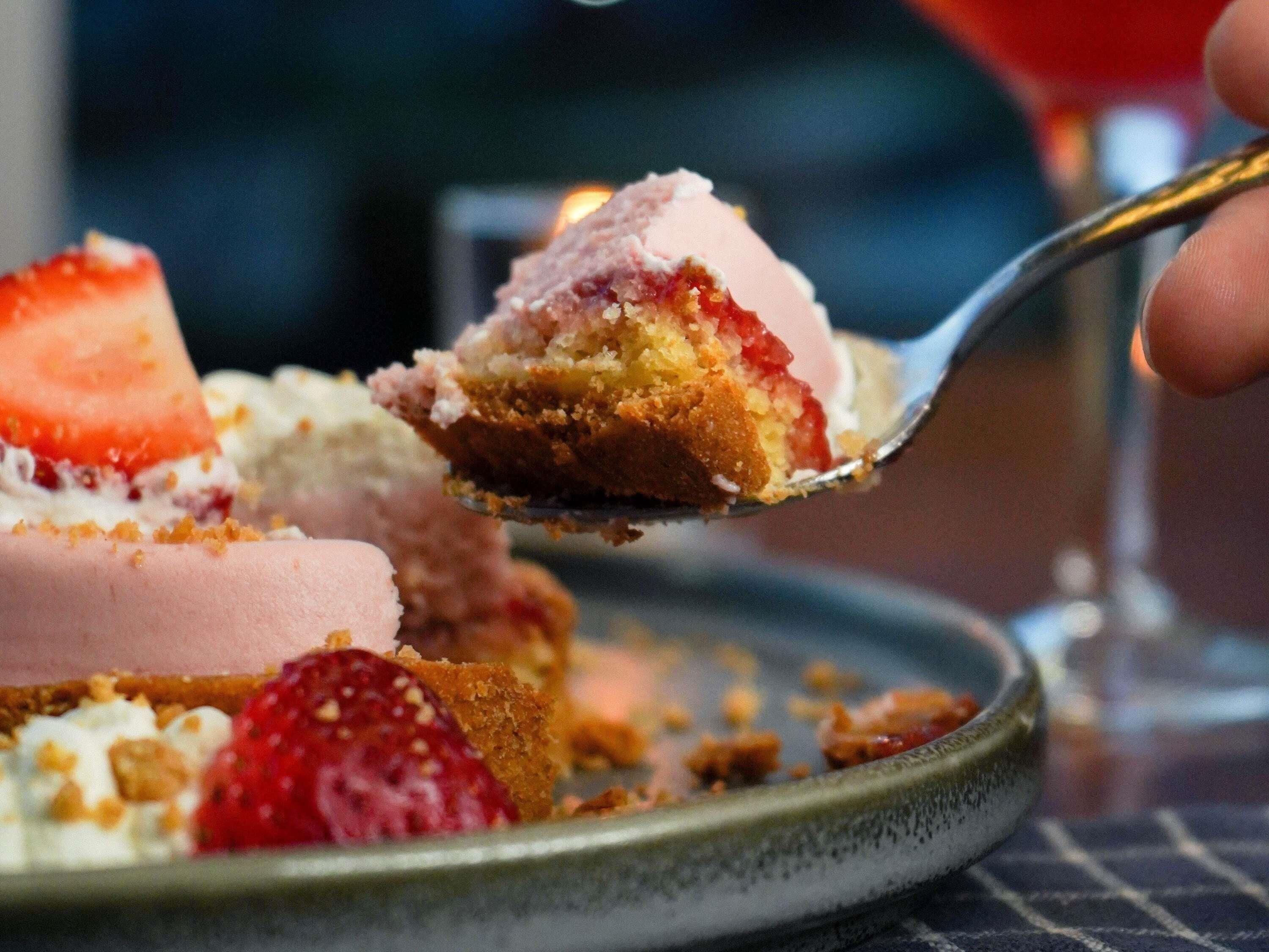A dessert with strawberries and a spoonful being lifted.