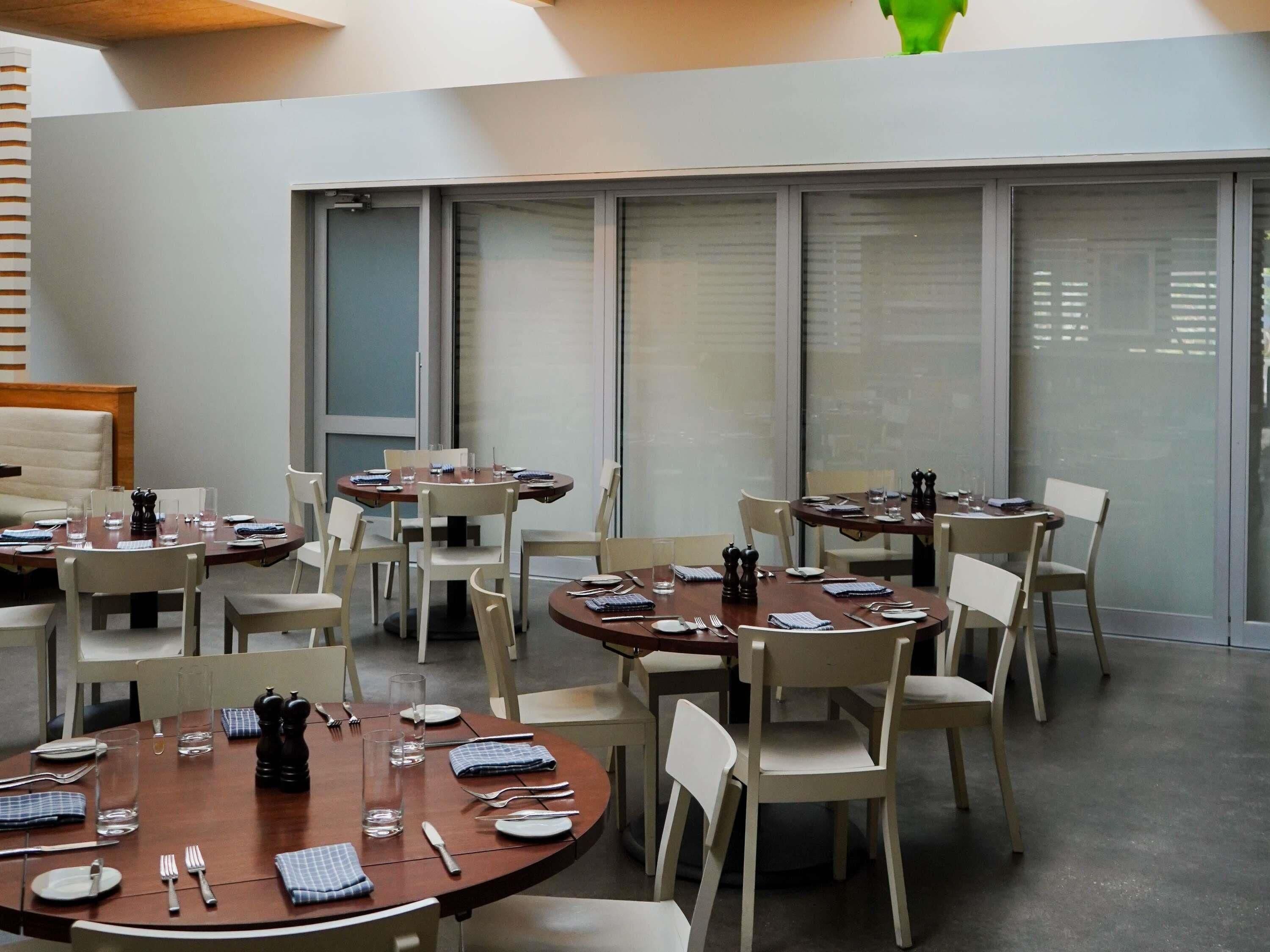 A modern dining area with multiple round tables, white chairs, and glass partitions.