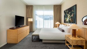 A hotel room with a bed, a TV on a wooden cabinet, a desk with a lamp, and a large painting on the wall. - 21c Museum Hotel Bentonville (Bentonville)