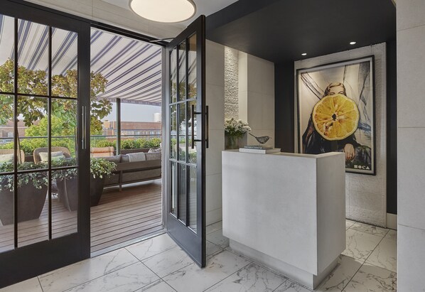 A reception area with a glass door leading to an outdoor seating area, a reception desk, and a large poster on the wall.