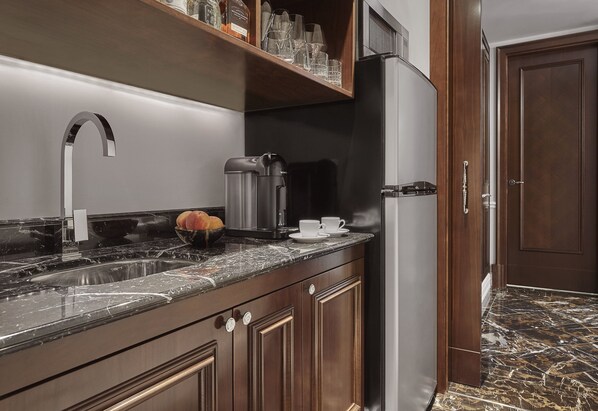 A kitchen with a marble countertop, stainless steel sink, and a refrigerator.