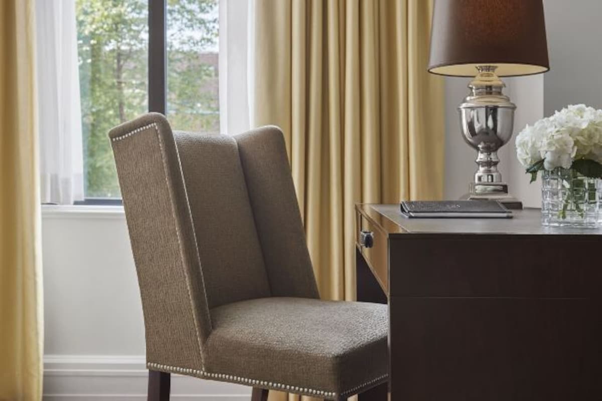 A chair with a high backrest and armrests, positioned in front of a desk with a lamp and a vase of flowers.