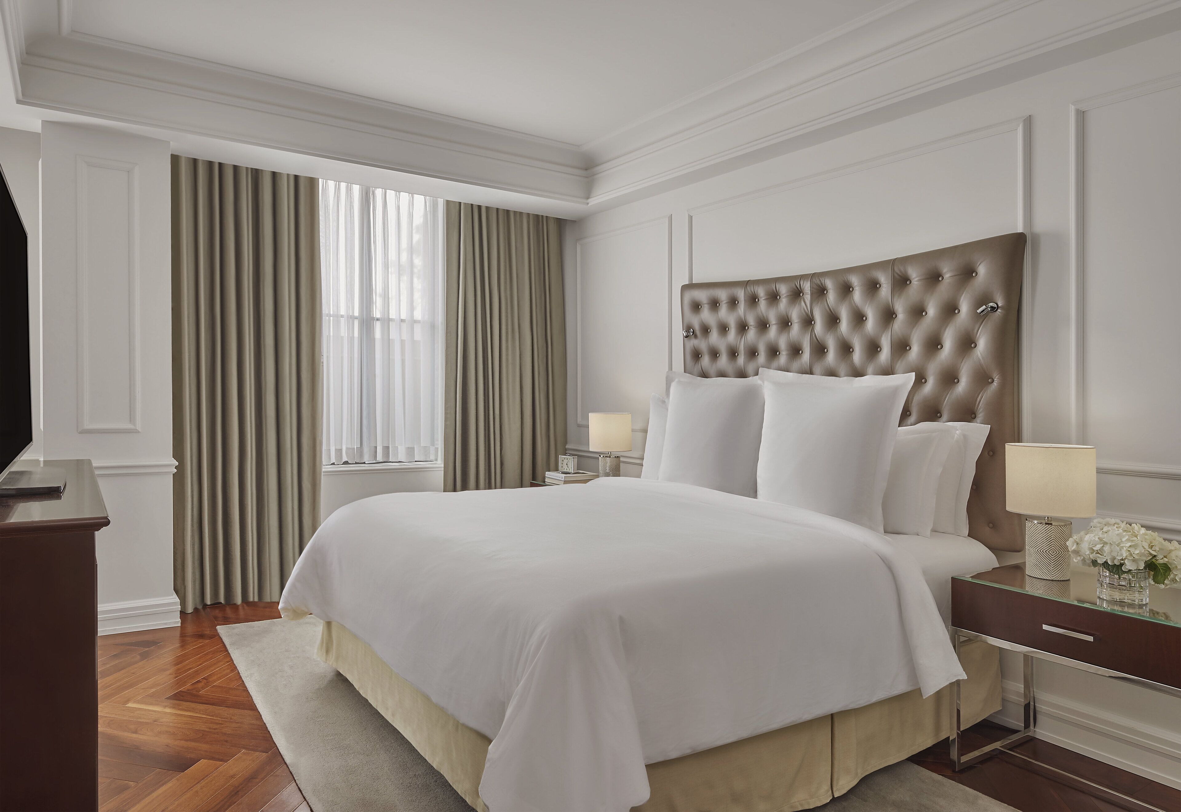 Habitación de hotel ordenada con una cama grande, una mesita de noche con lámpara y un aparador.