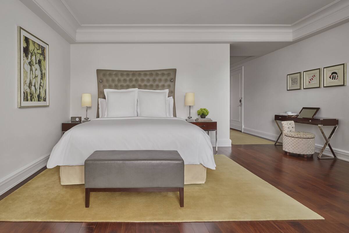 A neatly arranged bedroom with a large bed, bedside tables, a bench, and a desk with a chair.